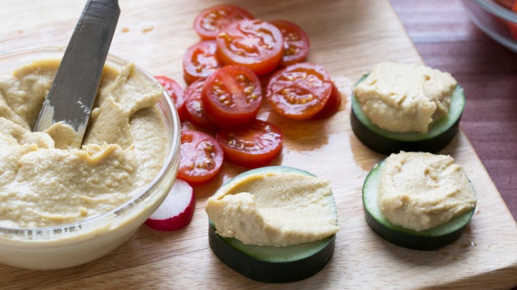 Cucumber with hummus and tomatoes beside a bowl of hummus. Eating regularly as a means to overcome binge eating.