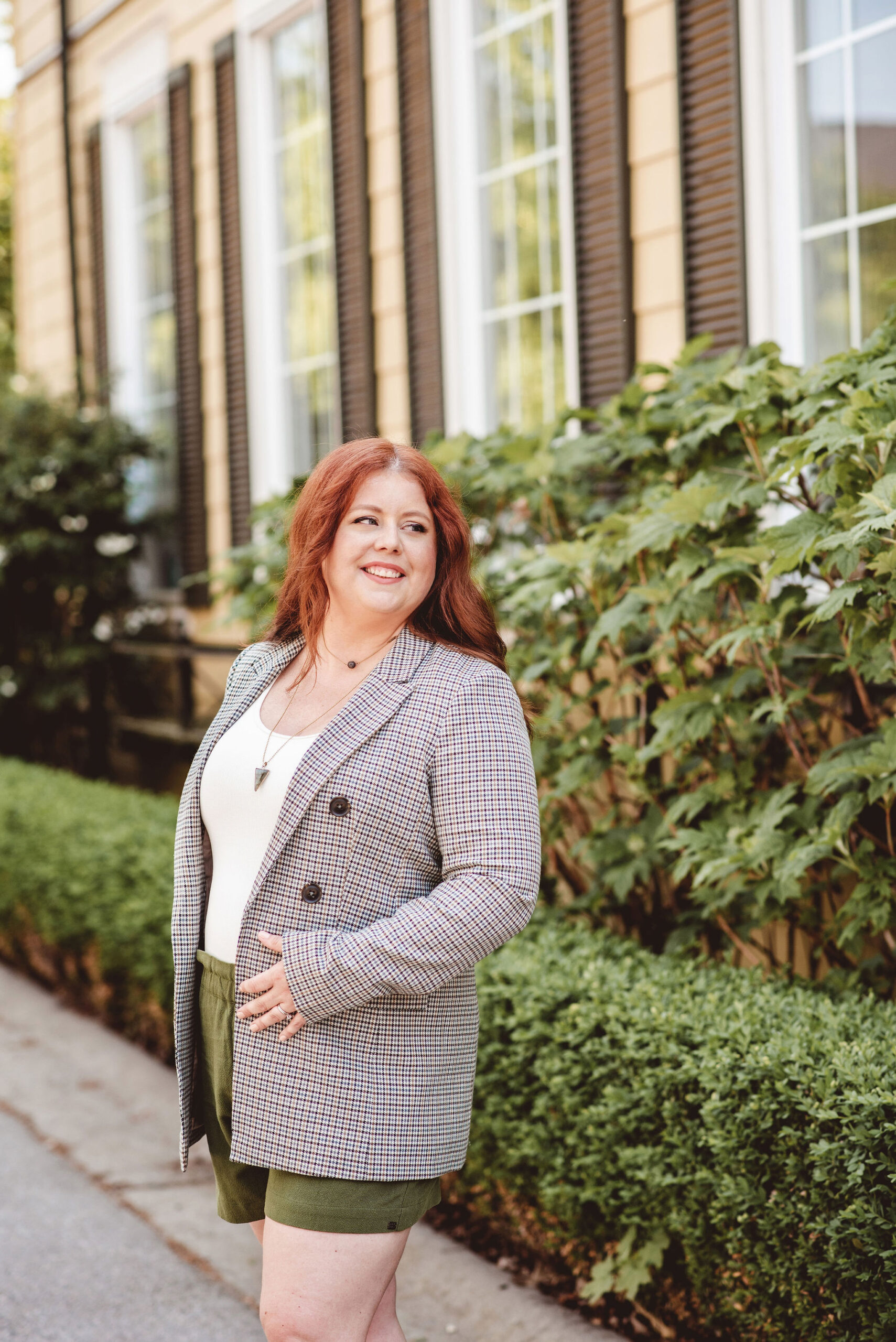 a woman wearing a stylish skirt and gray blazer outdoors smiling over their shoulder