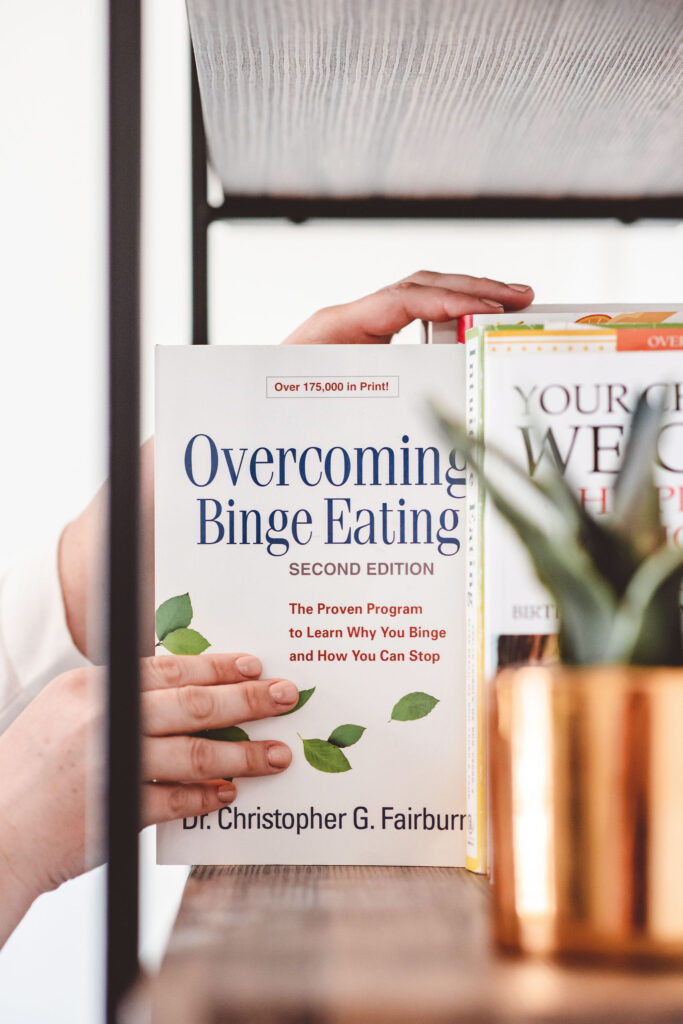 Person holding the book “Overcoming Binge Eating,” a resource for rebuilding hunger and fullness cues awareness.
