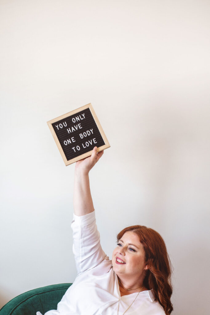 Woman holding sign that says "You only have one body to love," reflecting the real root of emotional eating.