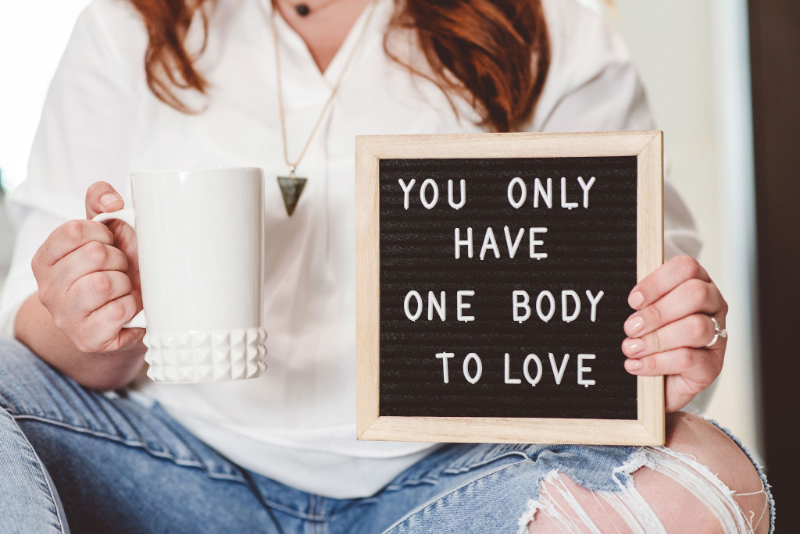 Woman holding sign “You Only Have One Body to Love,” finding food freedom message.