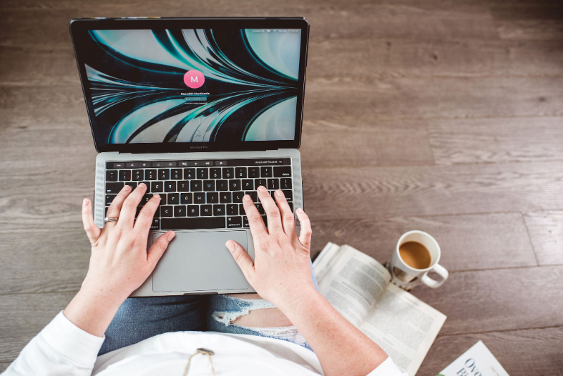 Person using a laptop with coffee and a book nearby, showing everyday scrolling habits and the impact of social media and body image