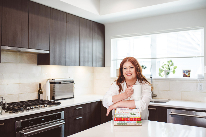 Woman in modern kitchen holding mug, smiling, representing how to feel satisfied after eating naturally