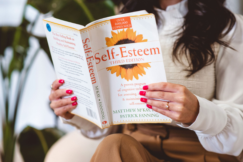 Person reading a self-esteem book to support body image healing, self-compassion, and a healthier relationship with themselves.