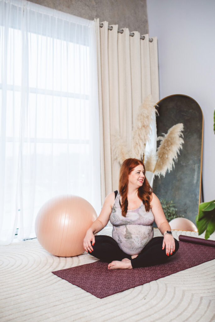 Woman sitting on a yoga mat practicing intuitive movement in a calm, welcoming exercise space.