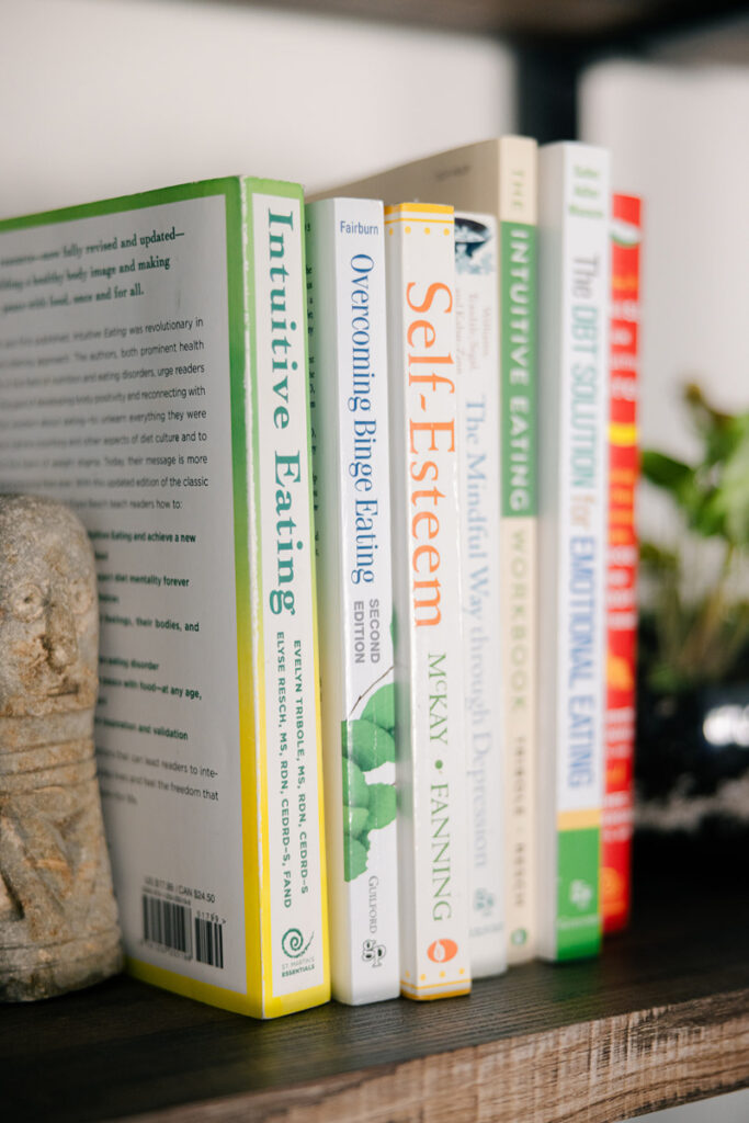 Books about intuitive eating and unconditional permission to eat on a bookshelf supporting food freedom.