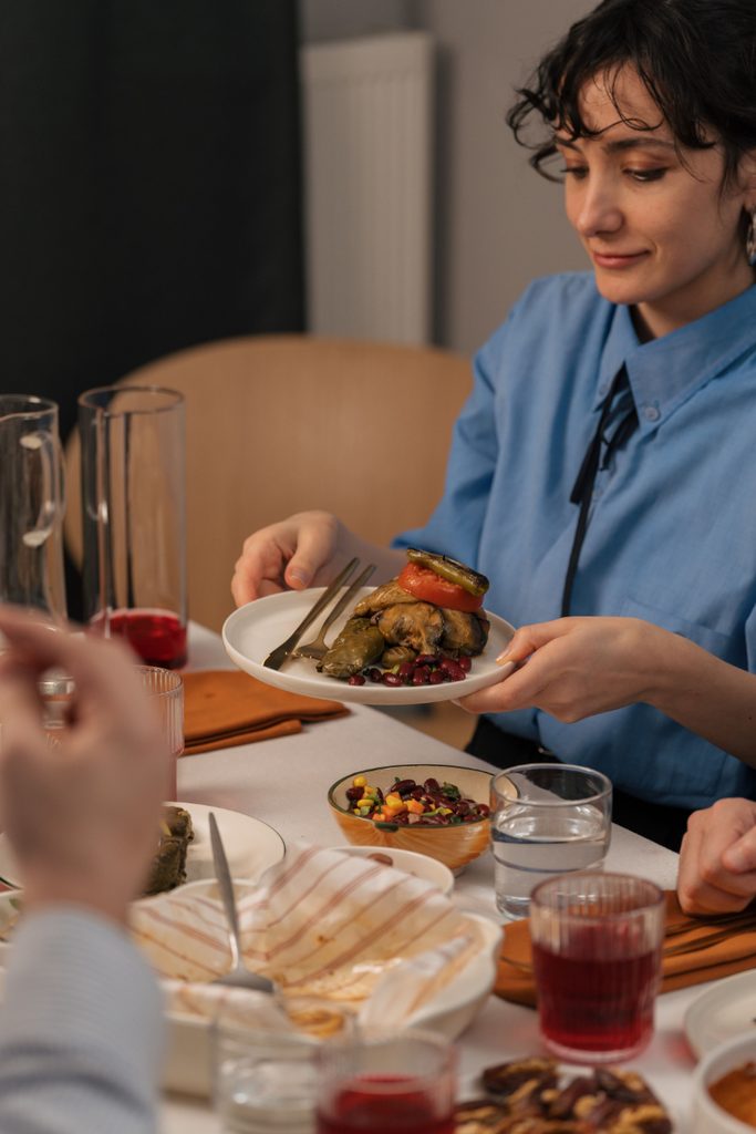 Person holding a plate of roasted food at a dining table with others, showing how eating normally can include shared meals and enjoying food.