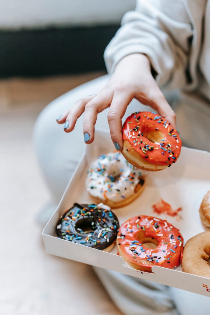 Hand reaching for a sprinkled donut from a box, illustrating how to stop the urge to binge eat.